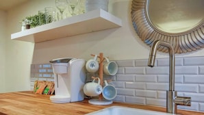 Une cuisine moderne avec un plan de travail blanc, une machine à café, un évier et un miroir décoratif.