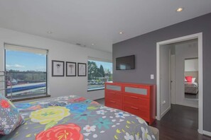 A bedroom with a large bed, a red dresser, a TV on the wall, and a window with a view of a park and buildings. - Large eclectic 1 BR above restaurant 15 min to PDX (Camas)