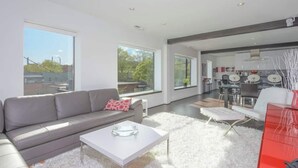 Una sala de estar moderna con un sofá gris, una mesa de centro blanca y un comedor con un aparador rojo.