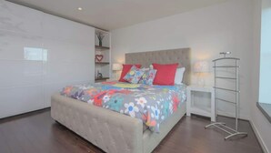 Un dormitorio moderno con una cama grande, una mesita de noche, una lámpara y un armario.