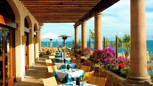 An outdoor dining area with tables and chairs, columns, and a view of the ocean. - Pueblo Bonito Sunset Resort, Cabo San Lucas, Mexico (Cabo San Lucas)