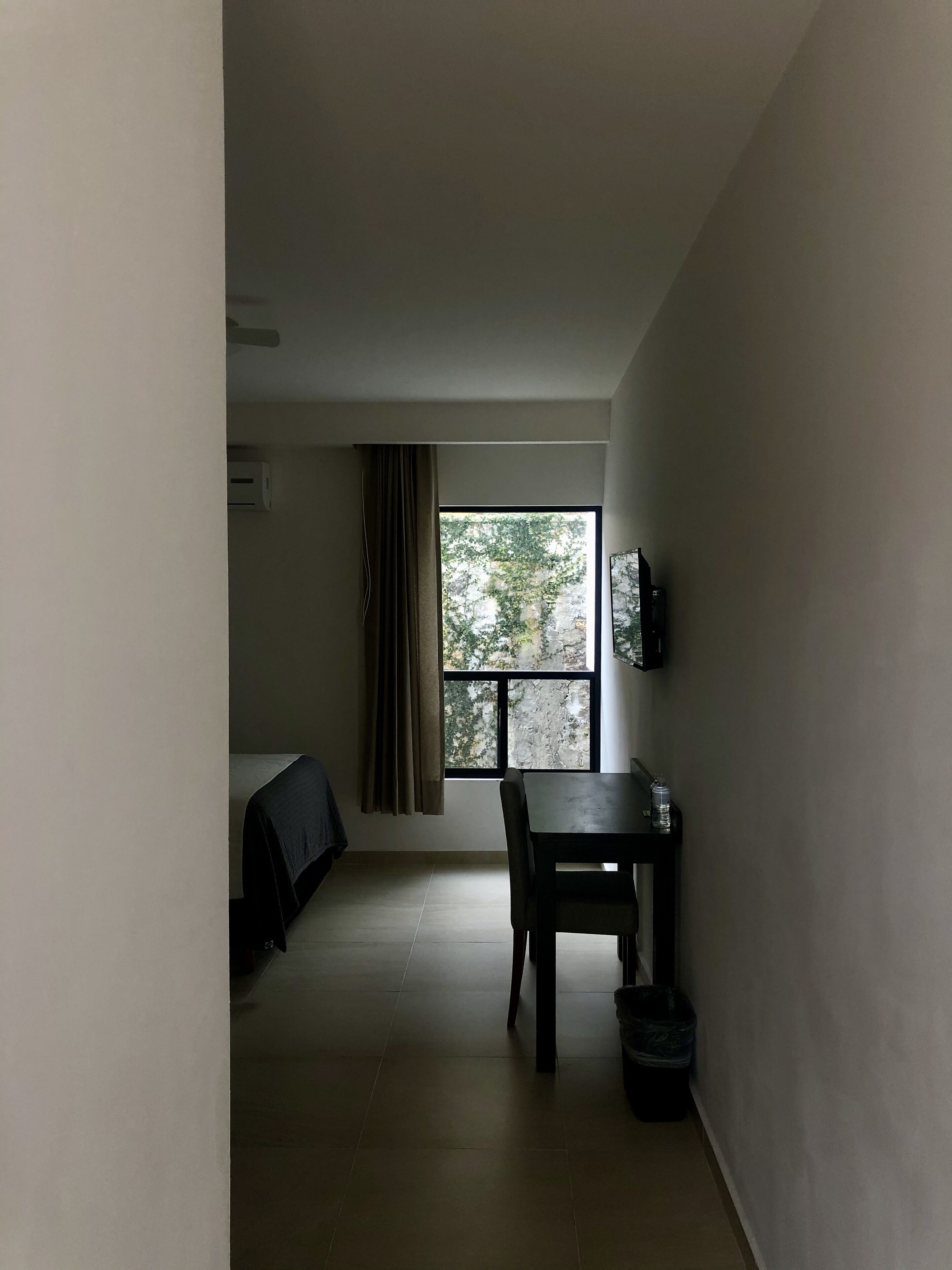 Una stanza con un'ampia finestra, un letto, un tavolo e una sedia.