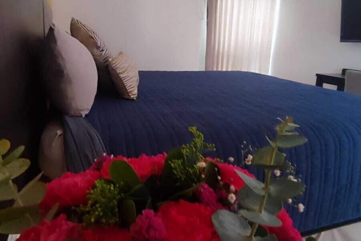 A bedroom with a bed, a ceiling fan, a window with curtains, and a wall-mounted air conditioner.
