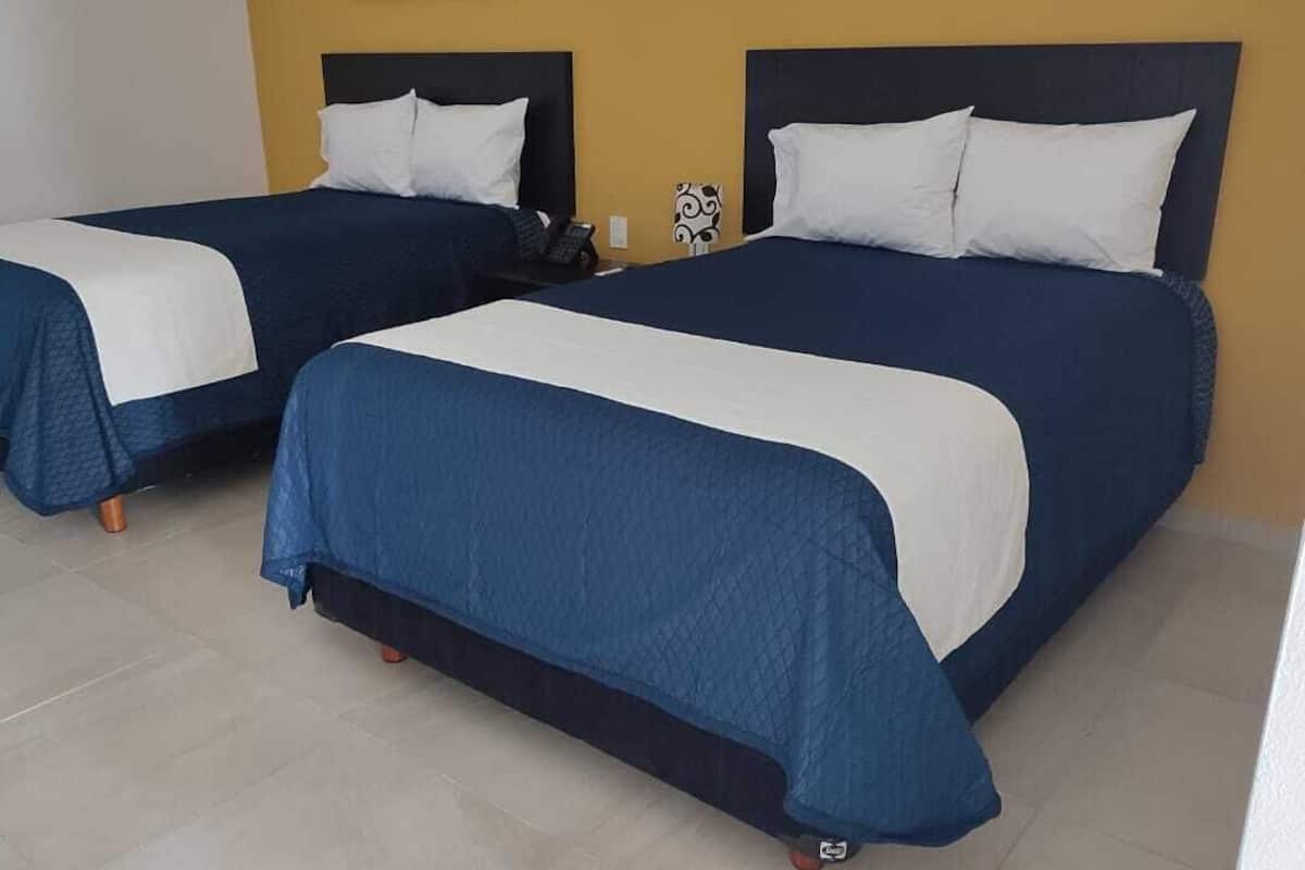 Two single beds with blue and white bedding, a telephone, and a decorative wall piece in a hotel room.