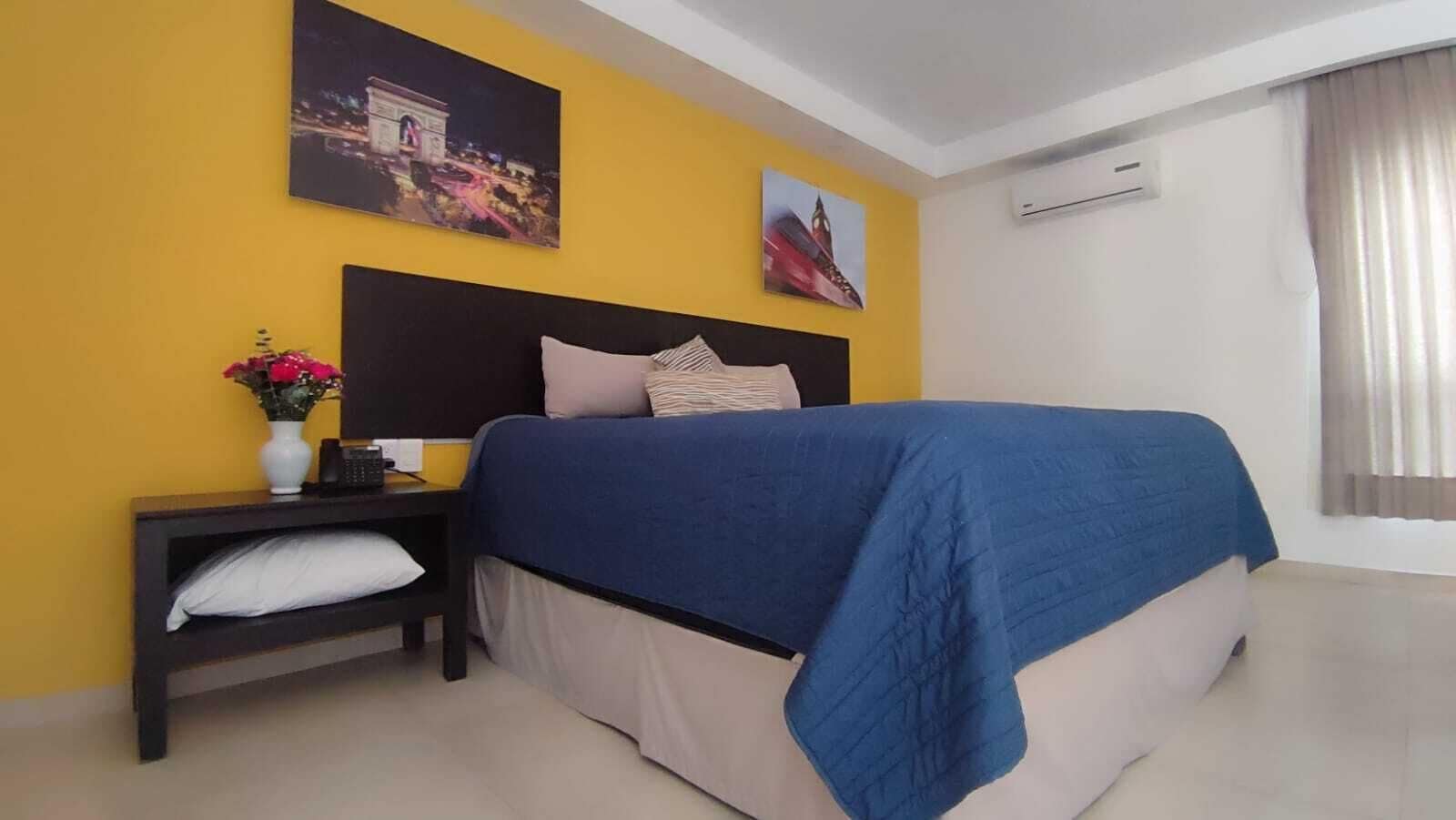 A hotel room with a bed, a nightstand, a vase with flowers, and two wall-mounted pictures.