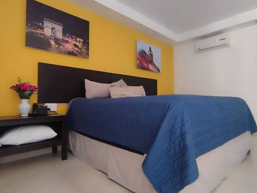 A hotel room with a bed, a nightstand, a vase with flowers, and two wall-mounted pictures.