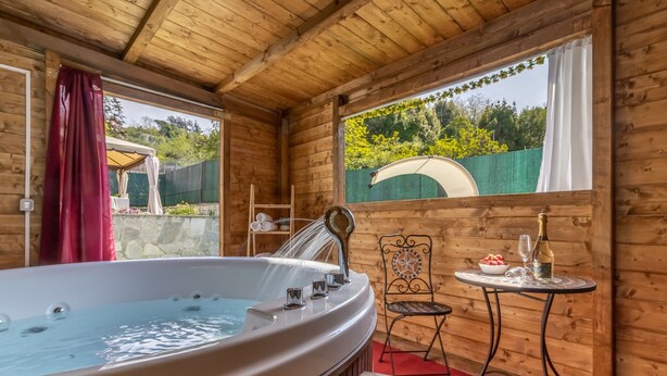 A wooden cabin with a hot tub, a table with drinks, and a chair. - Detached villa with outdoor hot tub, swimming pool and lawn  (La Spezia)