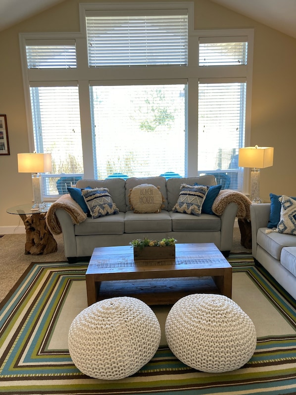 Ein Wohnzimmer mit einer Sofagarnitur, zwei runden Hocker, einem Couchtisch und einer Stehlampe.