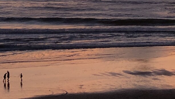Una playa con una gran formación rocosa silueteada contra el atardecer.