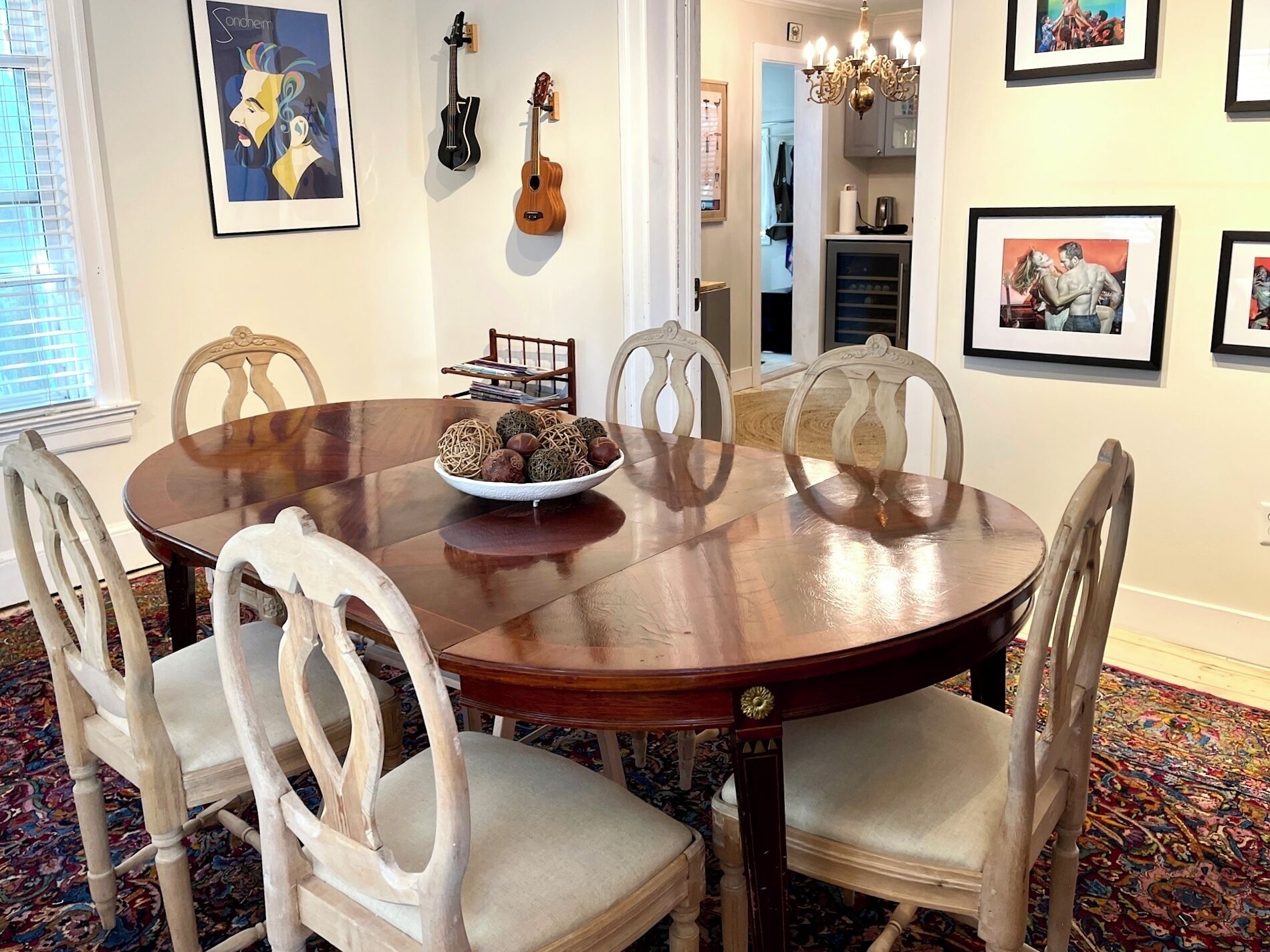 Une salle à manger avec une table ronde en bois, six chaises, un vase contenant des objets décoratifs et des œuvres d’art encadrées accrochées aux murs.
