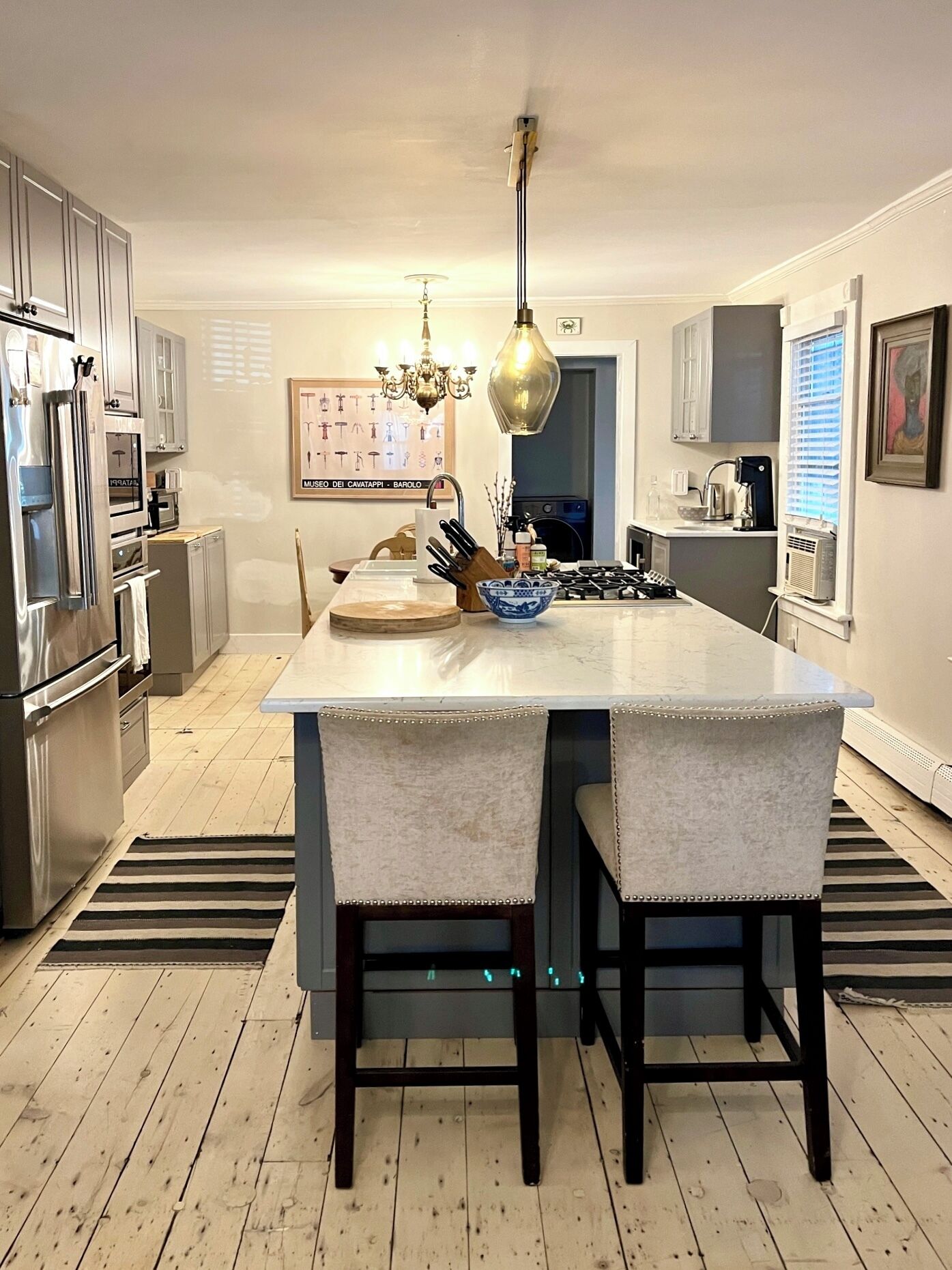 A modern kitchen with a central island, stainless steel appliances, and a chandelier.