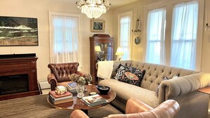 Un salon avec une cheminée, des fauteuils en cuir, un canapé, une table basse avec des livres et un vase, et un lustre.