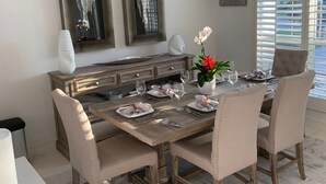 Una sala da pranzo con un tavolo di legno apparecchiato per quattro persone, circondato da sedie imbottite. Sulla parete sopra il tavolo si trovano due grandi dipinti astratti.