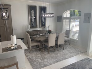 A dining area with a wooden table, white chairs, and a chandelier. There are two wall-mounted light fixtures above the table.