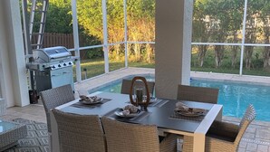 Zona pranzo all'aperto con vista piscina, sedie in vimini e barbecue.