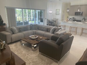 A modern living room with a sectional sofa, a coffee table, and a kitchen area with bar stools.