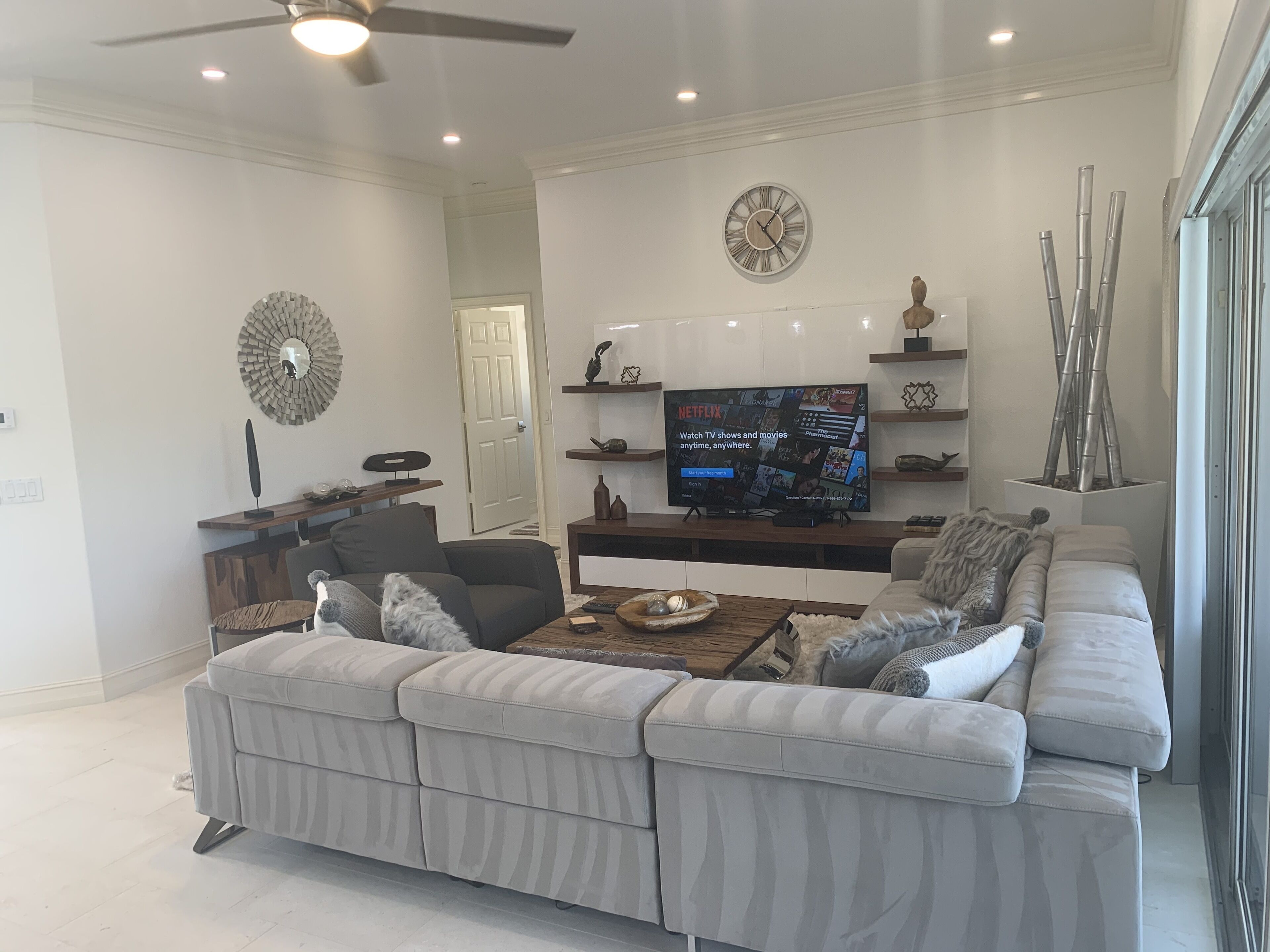 A modern living room with a sectional sofa, a flat-screen TV, and decorative items on shelves.