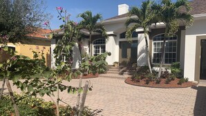 Una casa con vialetto lastricato, palme e un giardino con diverse piante.