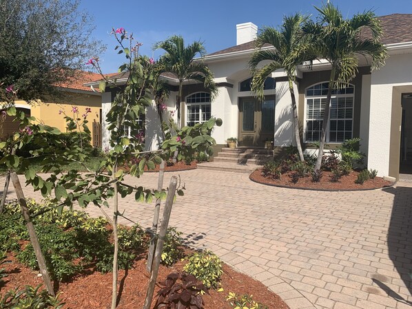 A house with a paved driveway, palm trees, and a garden with various plants. - AAA - MARCO ISLAND LUXURY HOME, WALK TO THE BEACH. (Marco Island)