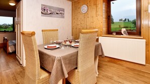 Un comedor con una mesa de madera dispuesta para cuatro, sillas de mimbre, un reloj en la pared y una ventana con vistas al verdor.