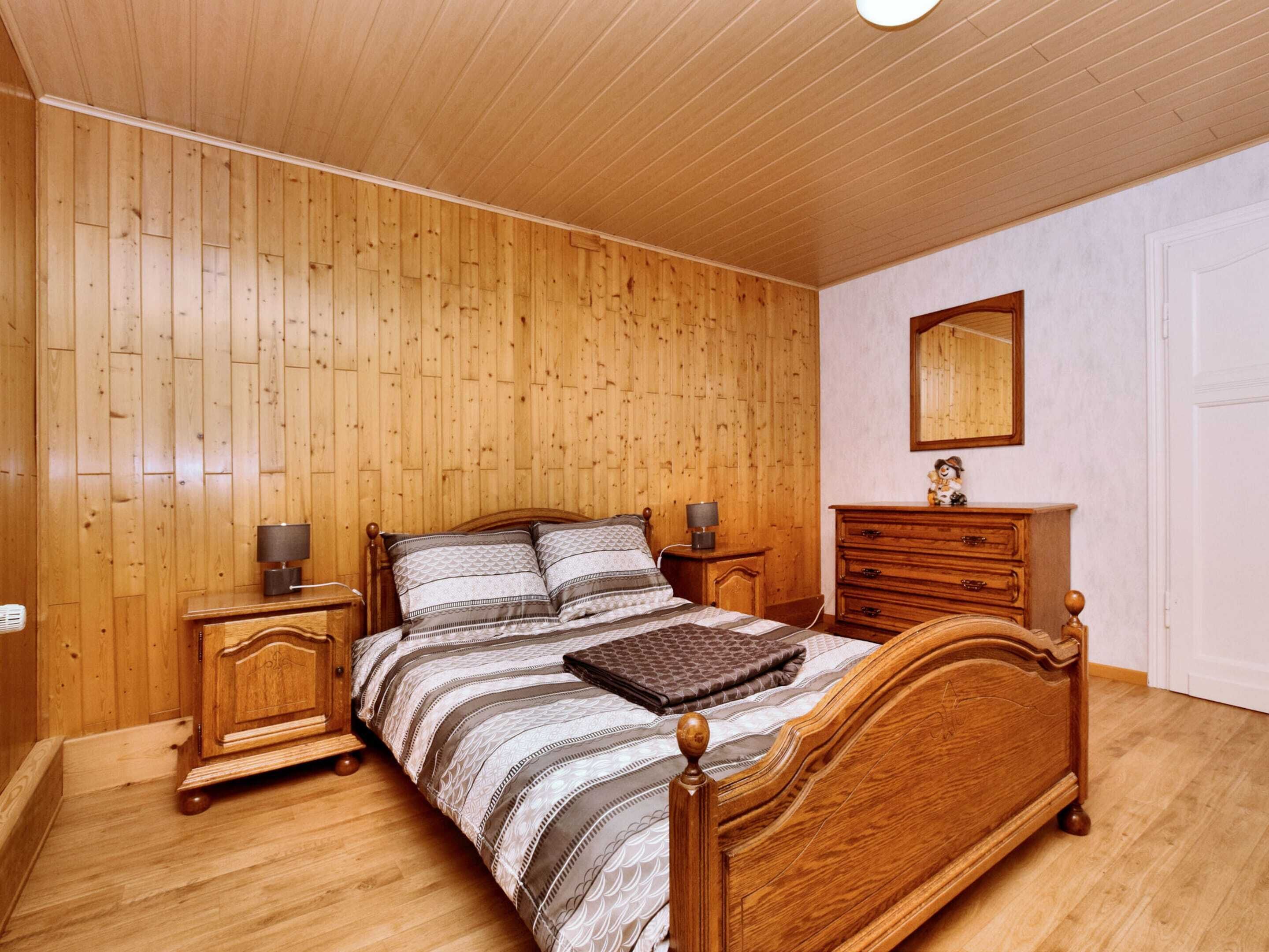 Ein Schlafzimmer mit Holzwänden, einem Bett, Nachttischen, einer Kommode und einem Spiegel.