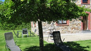 Un espacio al aire libre con césped, un árbol, dos sillones de descanso y un edificio de piedra al fondo.