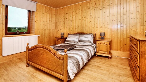 Un dormitorio con paneles de madera, una cama, mesitas de noche, un aparador y una ventana con vistas.