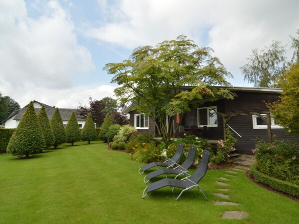 A residential property with a well-maintained lawn, a large tree, and a modern house with multiple windows and a dark exterior.