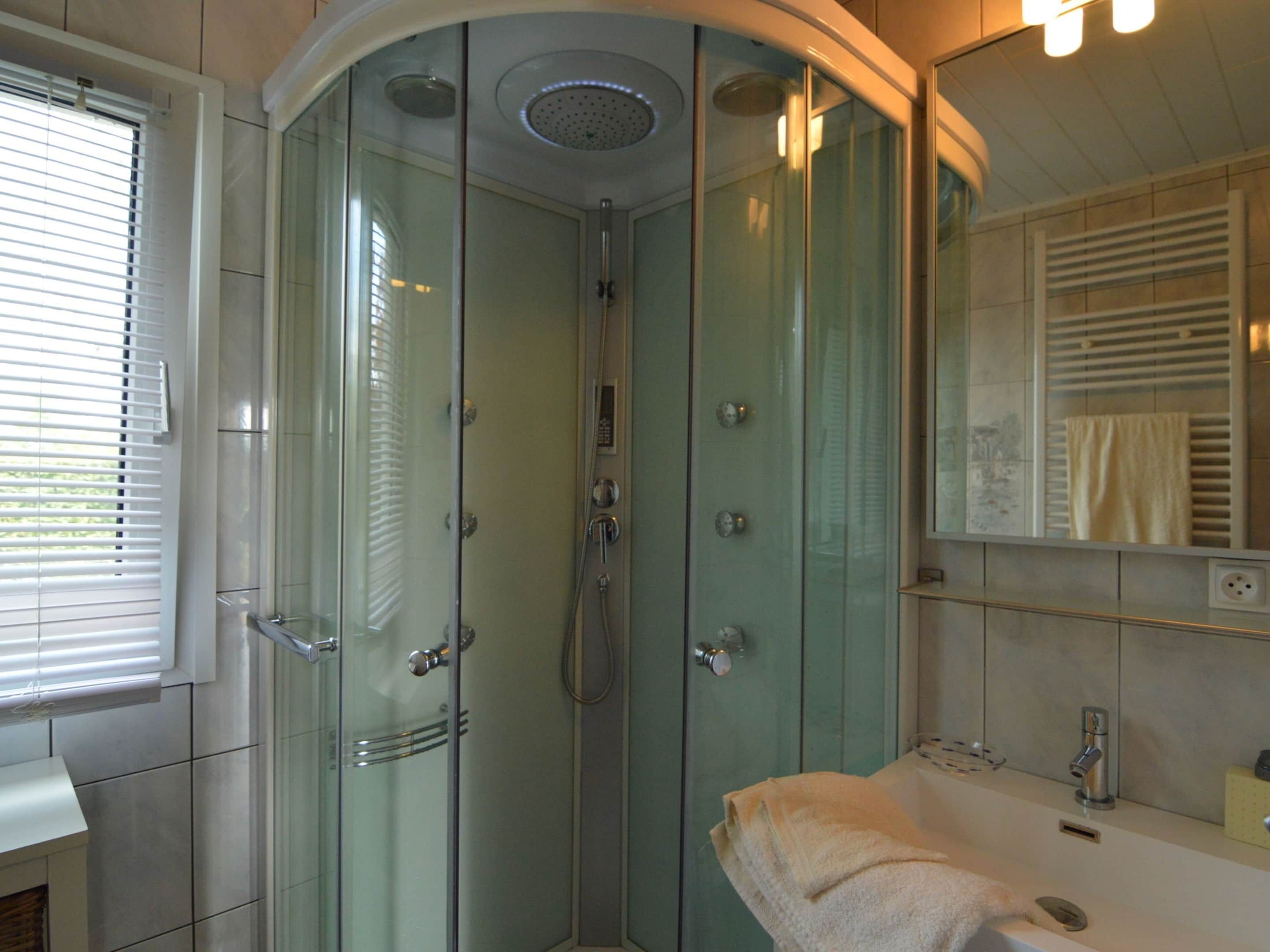 A modern bathroom with a glass-enclosed shower, a white sink, and a mirror with a towel hanging on the wall.
