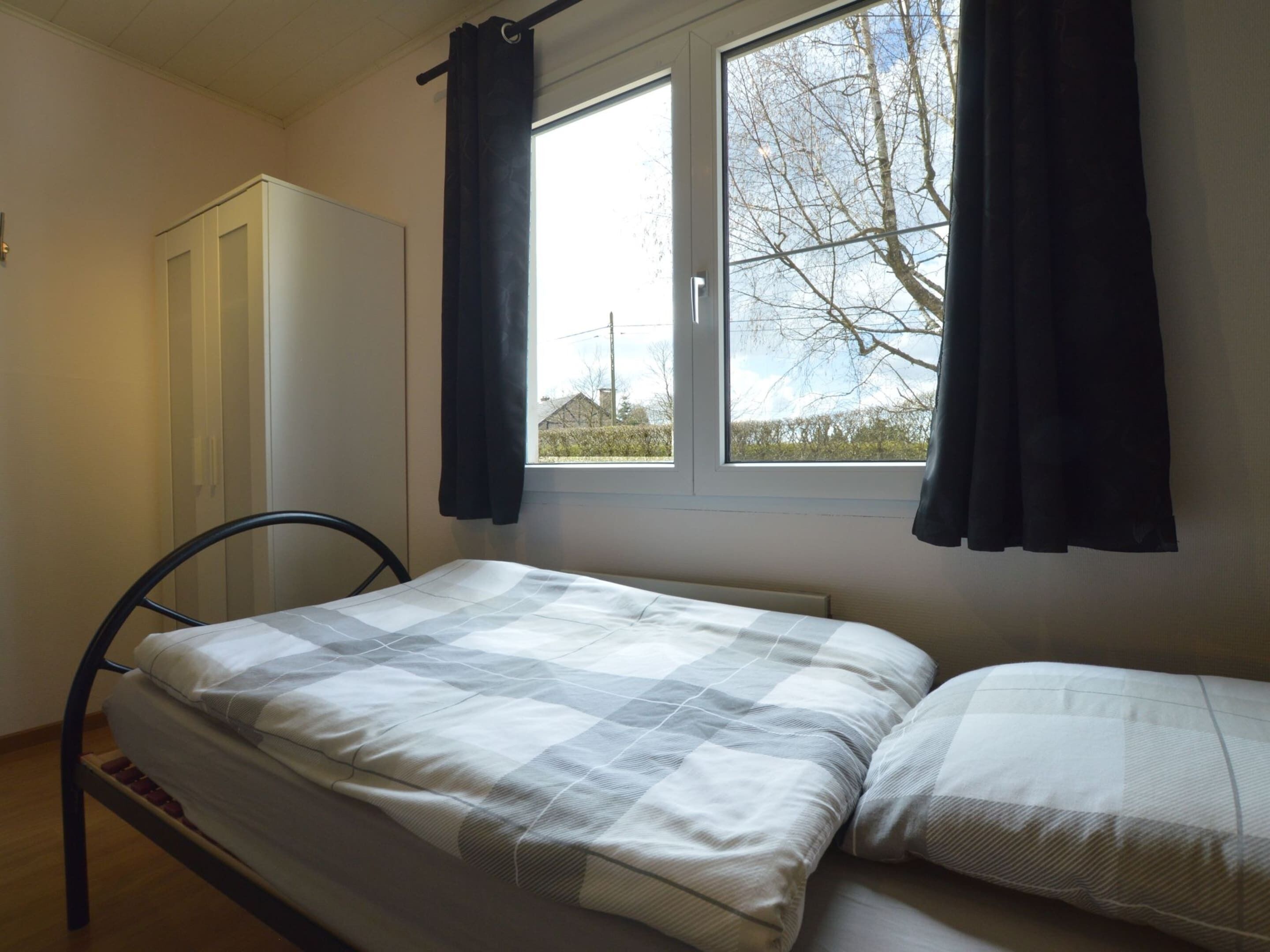 Una cama individual con una colcha a cuadros en una habitación con ventana, un armario y una silla.