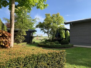 A well-maintained garden with a swing set, a stone barbecue, and neatly trimmed hedges.