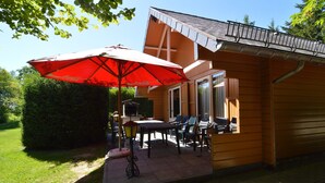Uma cabana de madeira com um alpendre, móveis de exterior e um guarda-sol vermelho.