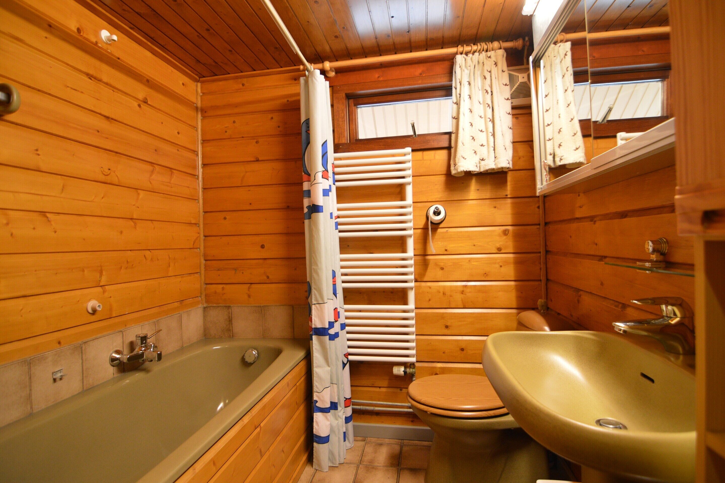 A wooden cabin bathroom with a bathtub, toilet, and sink.