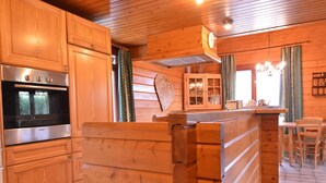 Interior de cabana de madeira com cozinha, incluindo forno Bosch, armários de madeira e mesa de jantar com cadeiras.