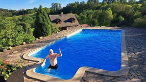 Une piscine bordée de pierres, entourée de verdure, avec une maison en arrière-plan.