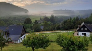 Un paysage rural avec des maisons, un champ d’herbe et une colline brumeuse en arrière-plan.