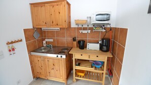 A compact kitchen with wooden cabinets, a stove, a microwave, and a coffee maker. - Retreat With Garden Views (Dolní Lánov)