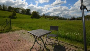 An outdoor patio with a metal table and chair, a brick floor, and a grassy field in the background. - Retreat With Garden Views (Dolní Lánov)