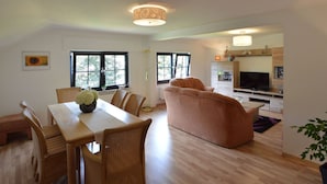 A spacious living area with a dining table, chairs, a sofa, and a television. - Apartment in Weywertz Near Ski Slopes (Buetgenbach)