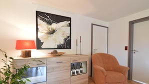 A modern living room with a wooden cabinet, a red lamp, a large abstract painting, and a comfortable orange armchair. - Apartment in Weywertz Near Ski Slopes (Buetgenbach)