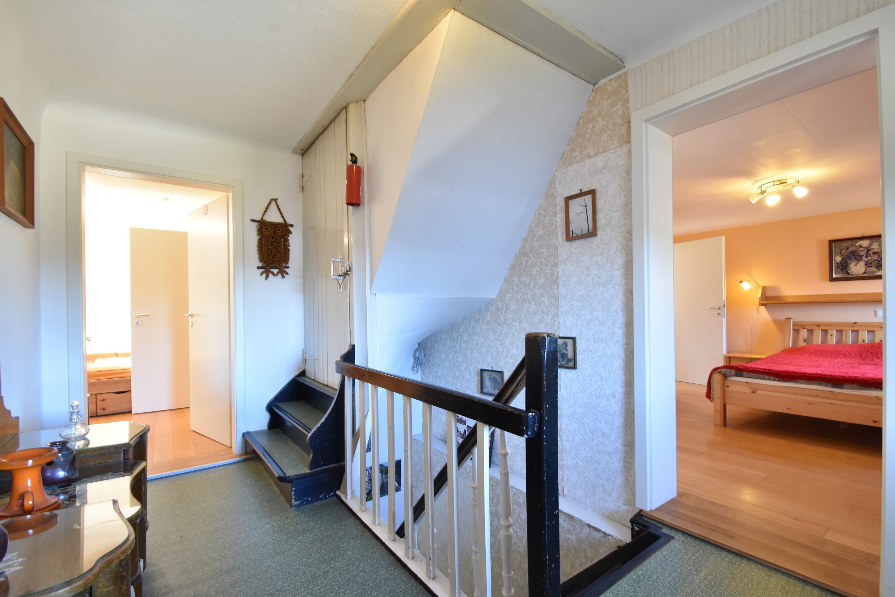 A staircase leading to a bedroom with a bed, a wooden floor, a door, and a wall-mounted light fixture.
