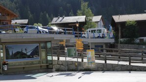 Un espace de stationnement avec un arrêt de bus et des panneaux de signalisation, entouré de bâtiments en bois et dominé par un paysage montagneux.