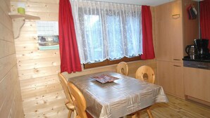 Une pièce aux murs lambrés, comprenant une table à manger, des chaises, un coin cuisine et une fenêtre avec des rideaux.