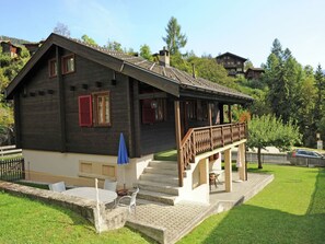 A wooden house with a balcony, a small outdoor seating area, and a staircase leading to the entrance.
