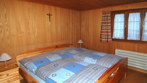 Une pièce en bois avec un lit, une table de chevet, une lampe, un radiateur et une fenêtre avec des rideaux.