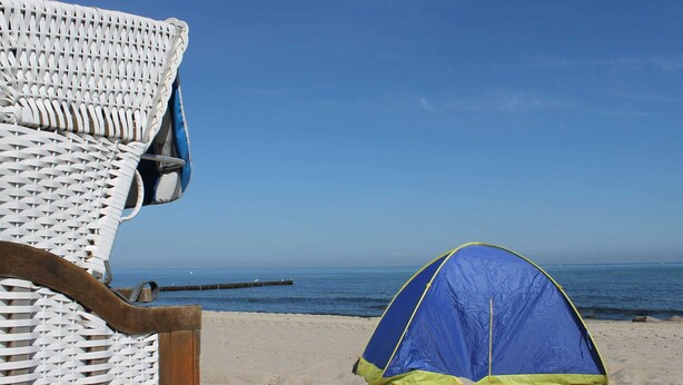 Escena de playa con una tienda azul y una silla de mimbre.