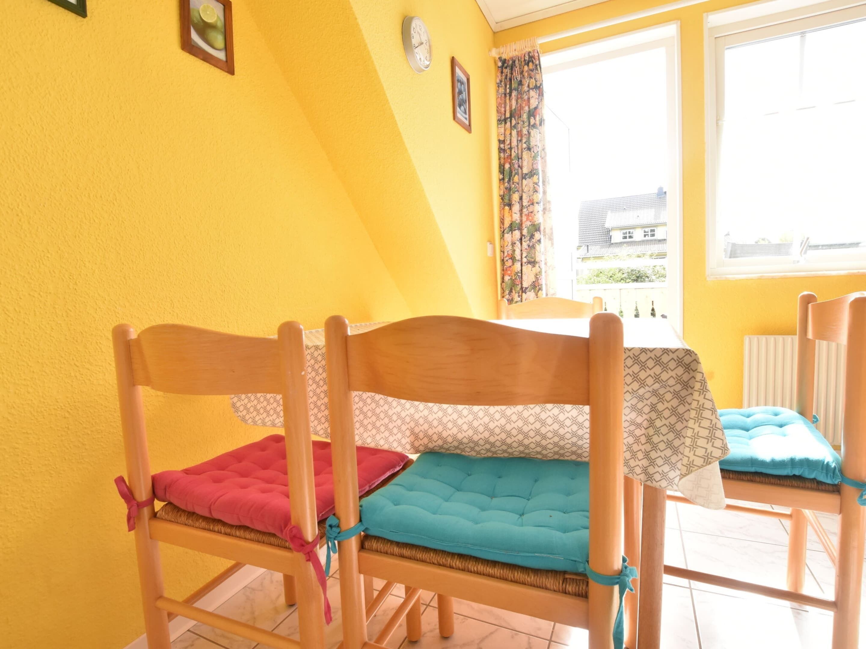 Una habitación con dos literas de madera, una ventana que da a una casa y una mesa con mantel estampado.