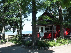 A red wooden cabin with a porch, surrounded by trees and a view of the water. - Lovely Holiday Home in Zierow With Terrace (Zierow)