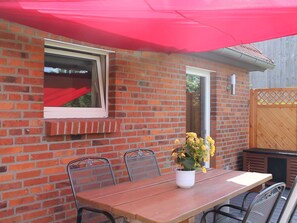 A patio with a brick wall, a wooden table, metal chairs, a potted plant, and a red umbrella. - Lovely Holiday Home in Zierow With Terrace (Zierow)