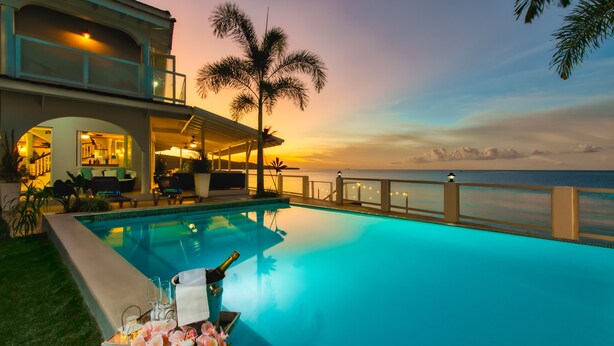 Uma área de piscina luxuosa com vista para o oceano, um espaço coberto para relaxar e um ambiente externo bem iluminado.